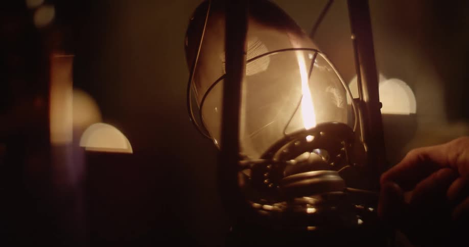 A person is turning up and adjusting the flame inside a lantern at night