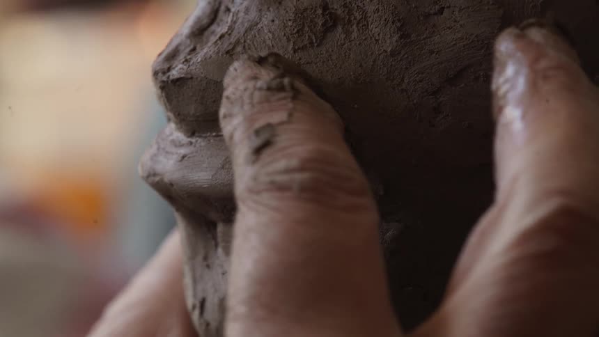 Person is sculpting lips on face made out of clay