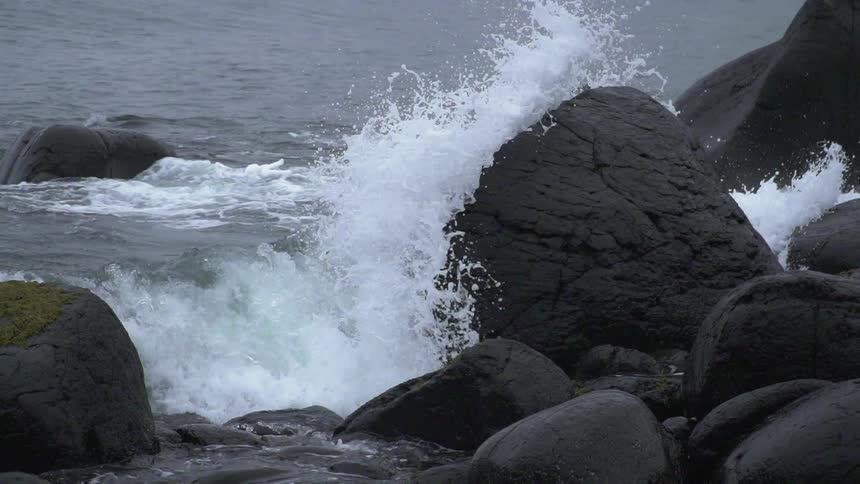 The large wave crashes against the rocks
