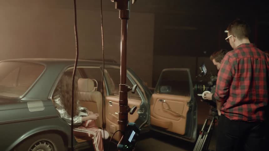 A woman sits in the backseat with door open while being filmed