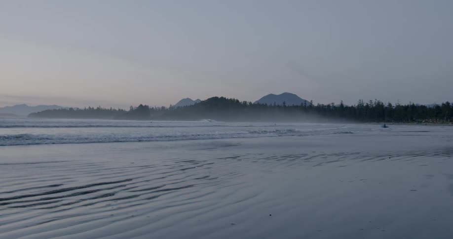 The waves slowly hit the sandy shore at sunset