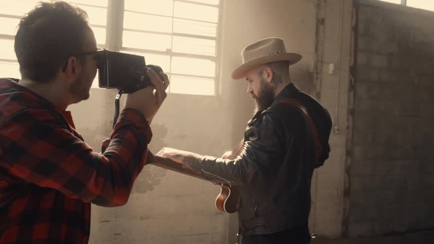 Man is recording another man playing the guitar in empty building