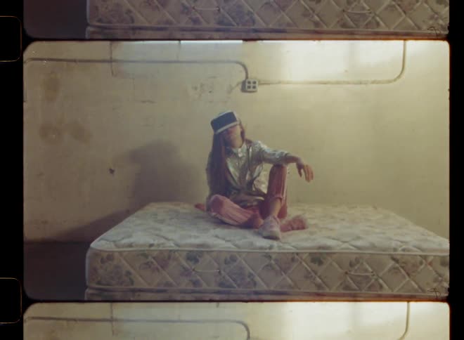 A woman is wearing a virtual reality headset as she sits on a mattress in daylight