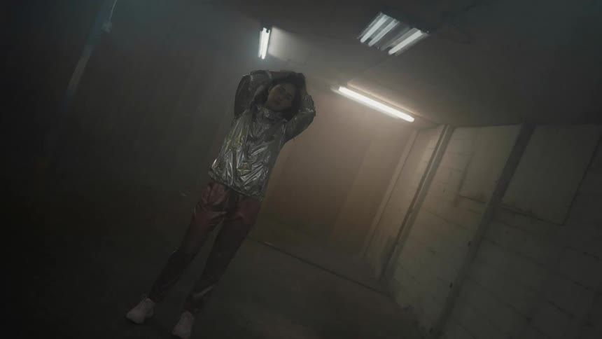 A woman stands in a room with her hands on her head and colored lights flashing