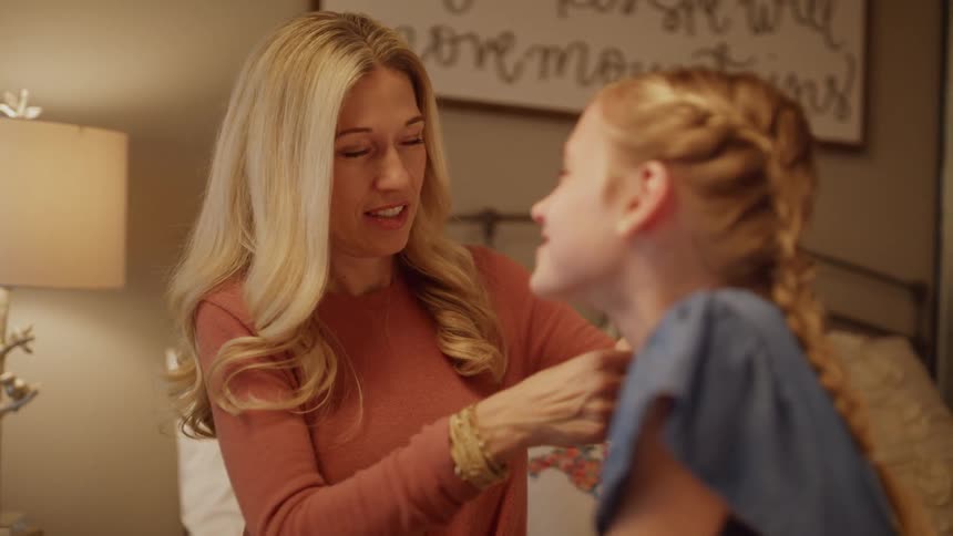 A woman smiles while braiding a girl's hair