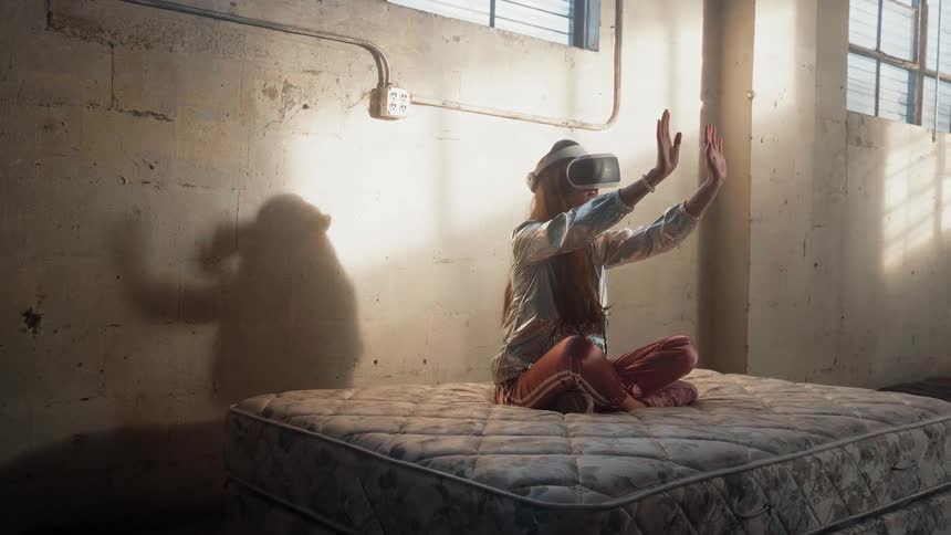 Girls uses virtual reality glasses and sits on a mattress in abandoned building