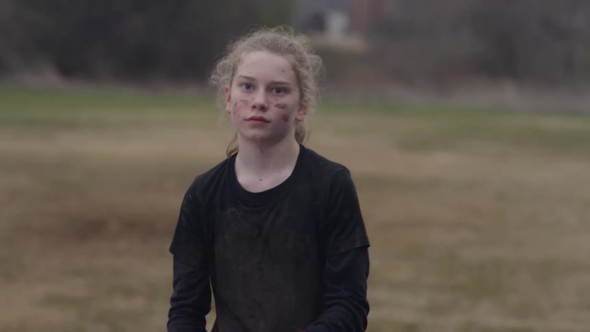 A girl with mud on her faces tosses and catches a football