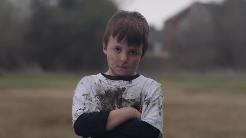 A boy with a muddy shirt and face crosses his arms