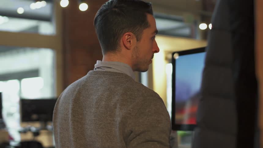 A man hangs his coat on a hook and starts working on a computer
