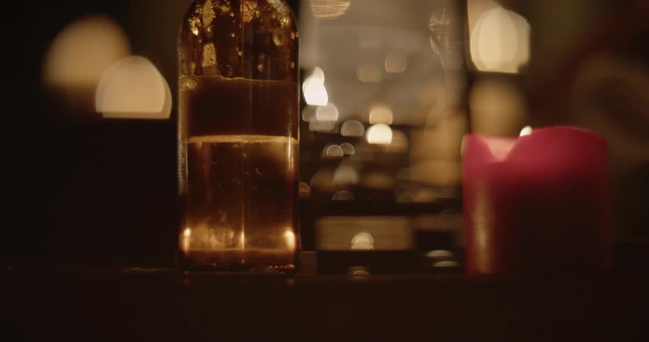 Person sets beer bottle down on table next to flickering candles