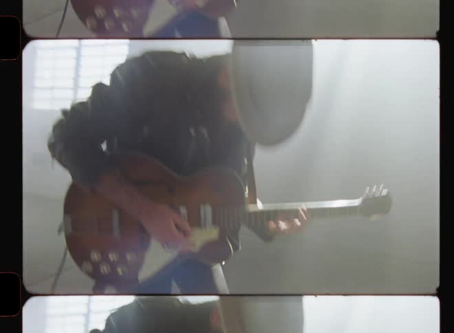 A man is playing a guitar inside an abandoned warehouse in daylight