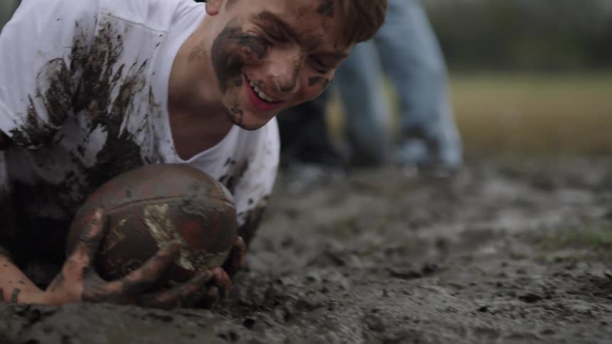 Kid playing football gets knocked down into the mud