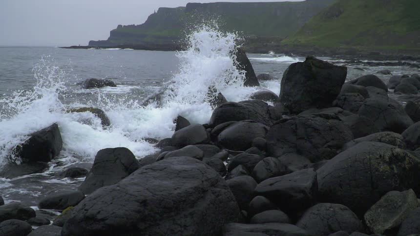 The waves splash against the large rocks by the shore