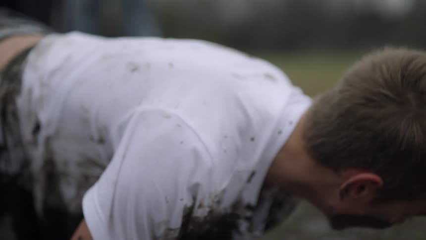 A boy holding a football falls into the mud with the ball