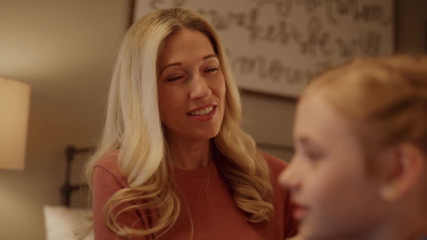 A mother is braiding her daughter's hair inside a bedroom