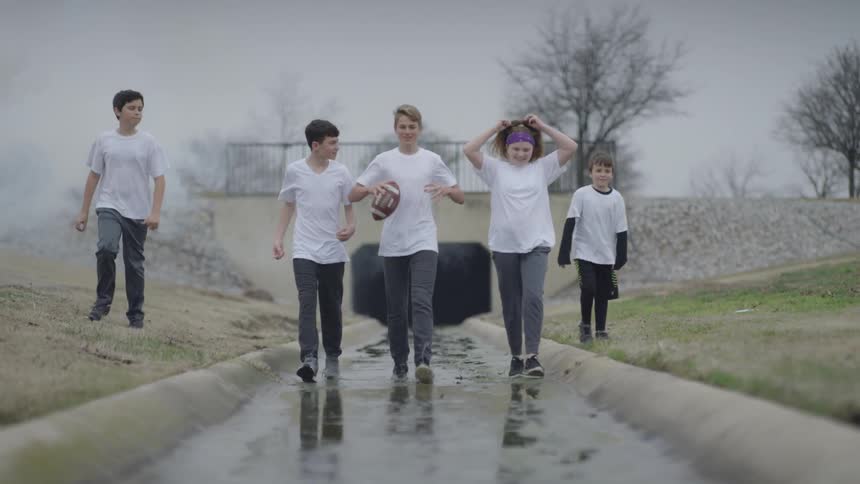 A group of teenagers walk outside with a football