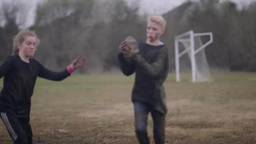 Teenagers play football in a muddy field