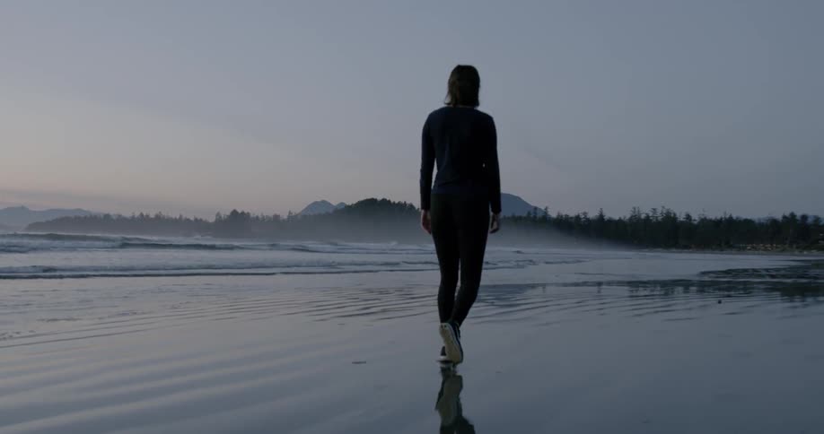 A woman walks on a beach at dusk