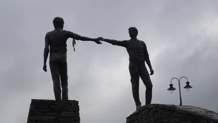Two statues reaching for each other on a cloudy day