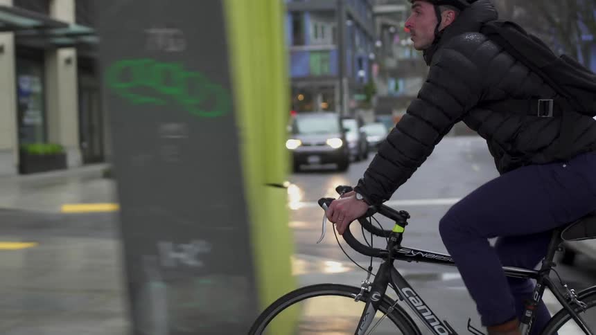 Man wearing helmet and backpack is riding bicycle on city street