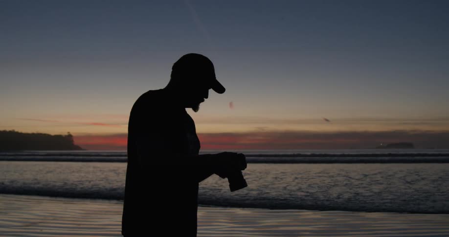 A man takes a photograph on the beach at sunset