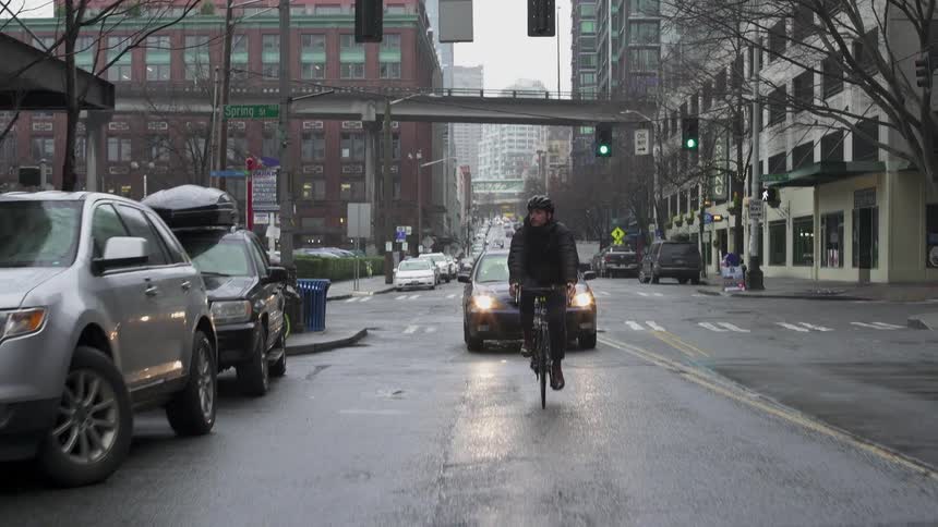 A man rides a bicycle on a city street with a car behind him