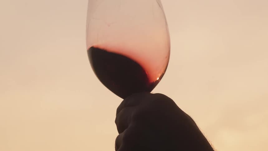 A man swirls wine in a glass at sunset