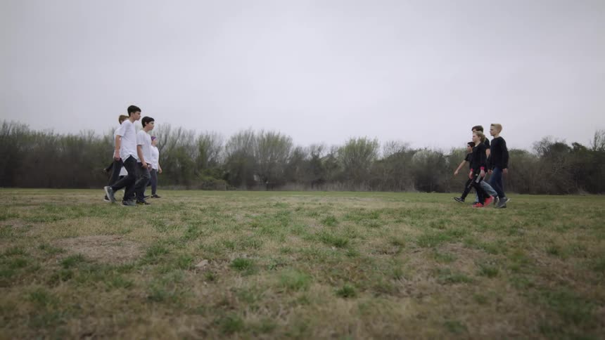 Group of kids in white shirts walk across a grassy field to meet a group of kids in black shirts