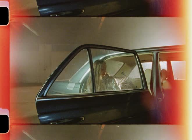 A woman is sitting with the door open in a car parked inside a building