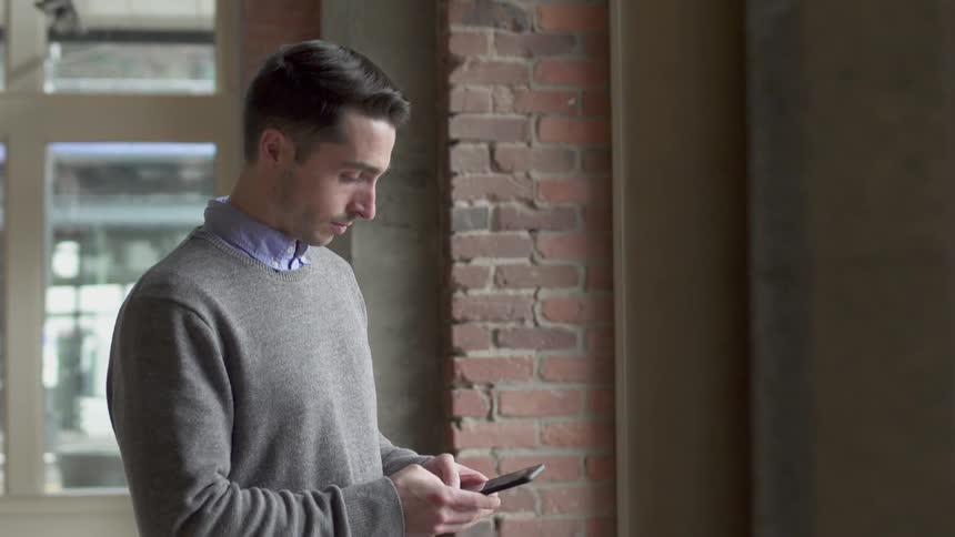 The man is typing on his phone by the window
