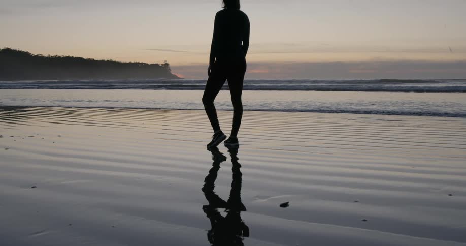 Woman is standing on ocean beach after sunset