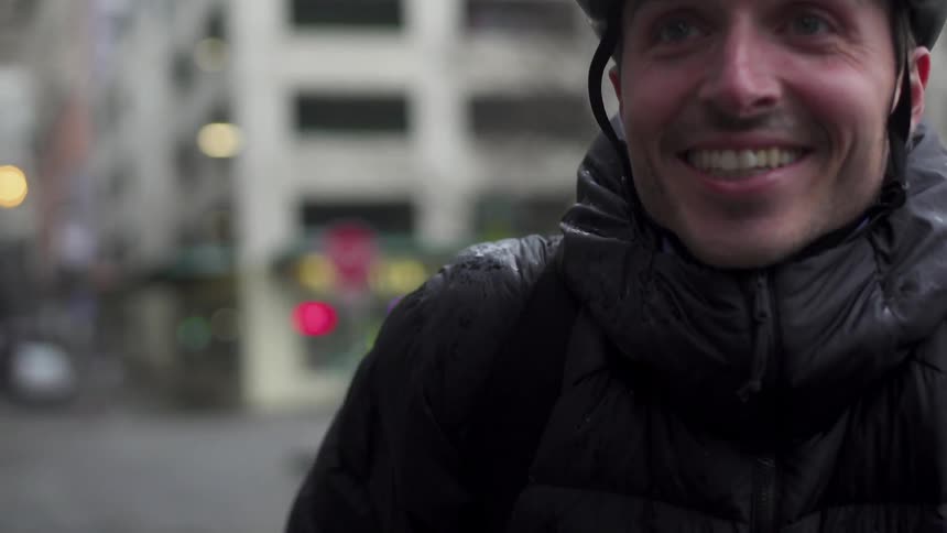 A man smiles as he stands in the rainy city