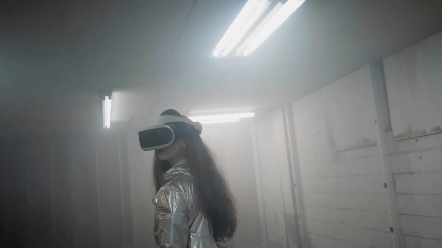 Woman in empty building is wearing virtual reality headset while lights flash