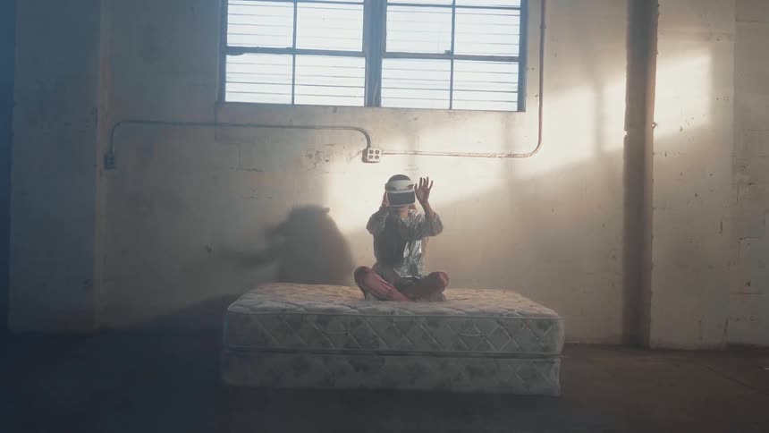 A person wearing a virtual reality headset sits on a mattress