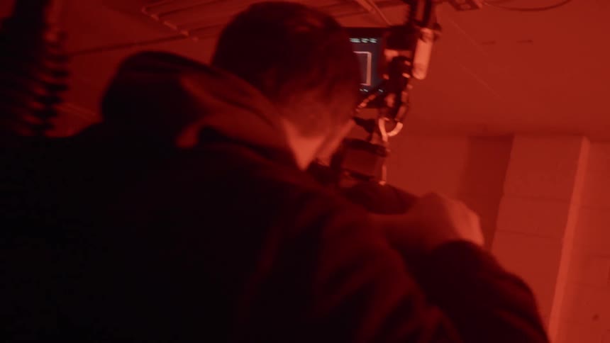 A cameraman films a woman standing with hands on head while lights flash