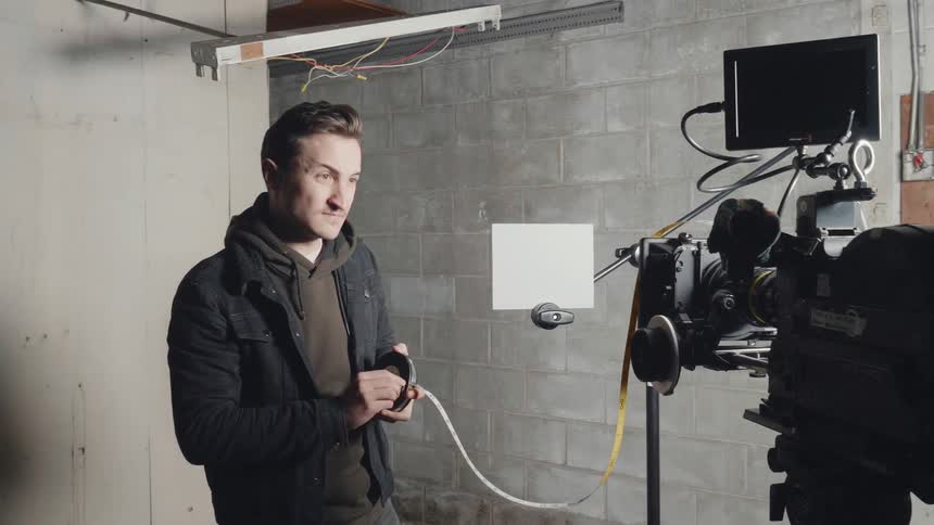 Man using a measuring tape to set the distance from a camera to its subject indoors