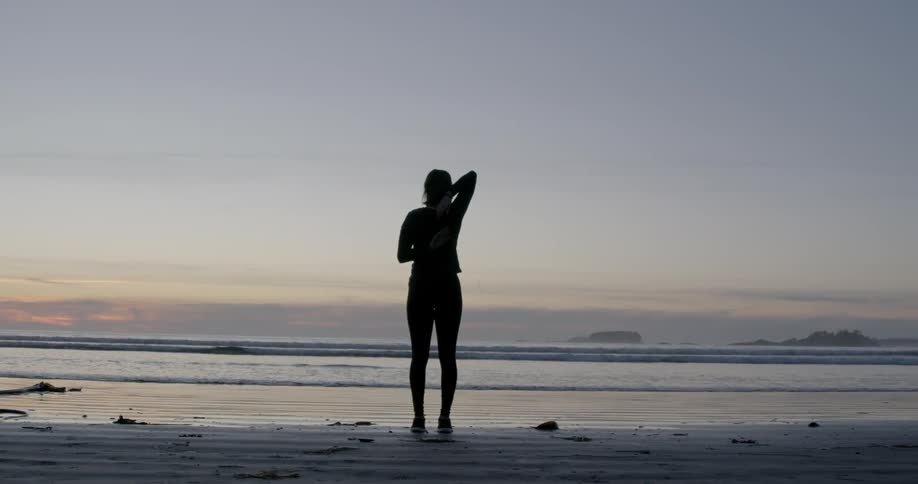 A woman stretches on a beach at sunset