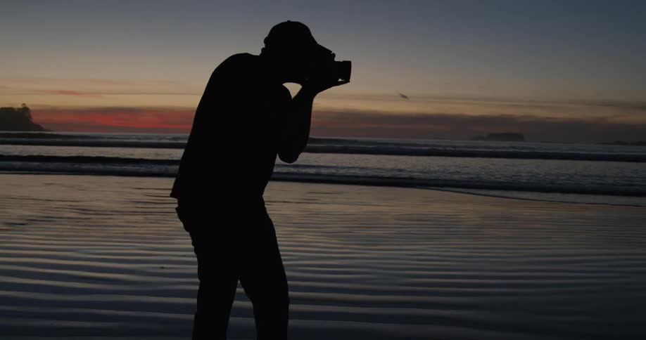 A photographer takes a picture on a beach at dusk