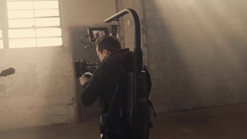 A guitarist is filmed playing in a dusty warehouse