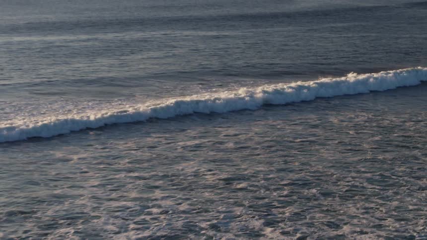 Foamy ocean waves coming towards the shore at sunset