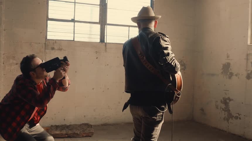 A man videotapes while a musician plays guitar