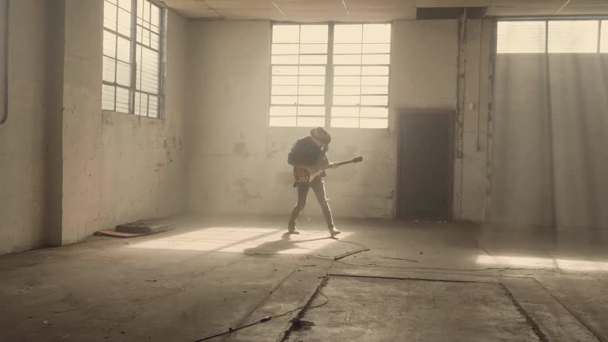 A man plays guitar in a dusty warehouse