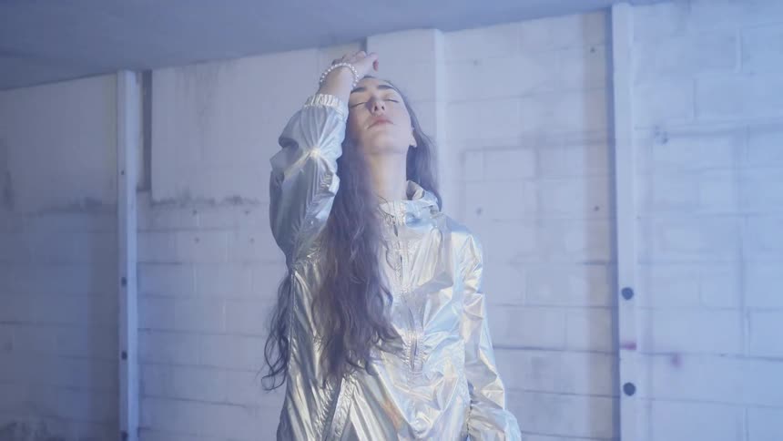Woman stands in strobe lit room and runs hands through hair