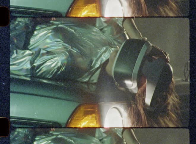 A woman wearing virtual reality goggles lays on the hood of a car at night