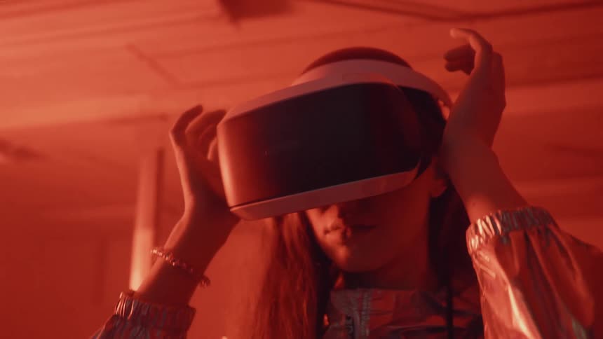 A woman is grasping at the vr headset she is wearing while standing inside a warehouse