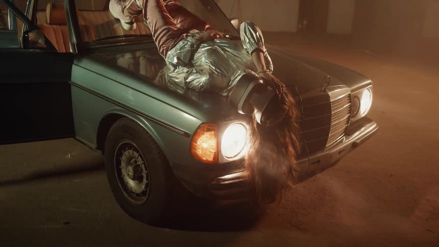 A woman is laying on the car hood wearing a virtual reality headset