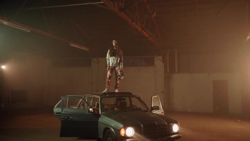 A woman stands on the roof of a parked car at night