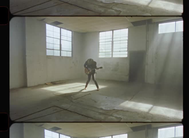 A man is playing a guitar inside an abandoned warehouse in daylight