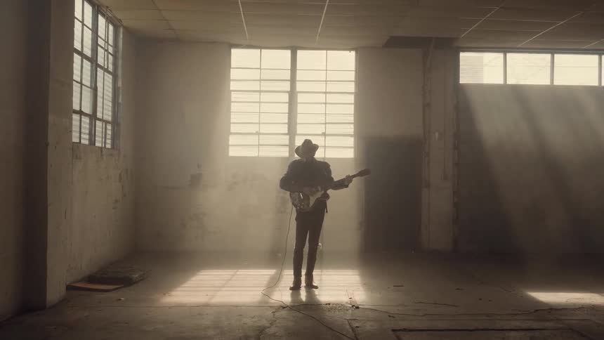 Man in empty building is playing guitar near sunny window