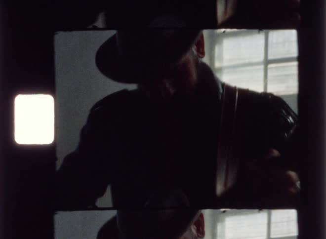 A man wearing a hat plays guitar in a dark room